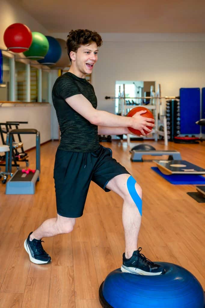 Jongen traint met een bal op een balanskussen in de oefenzaal